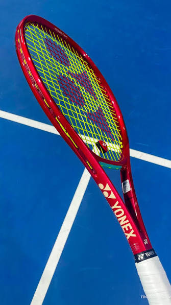 Roter Yonex VCORE Tennisschläger auf blauem Tennisplatz mit gelber Saite.